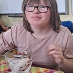 Uczennica siedzi przy stole i je lody z pucharka.
