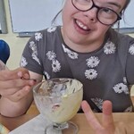 Uczennica siedzi przy stole i je lody z pucharka.