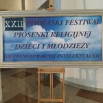 Plakat w ramie z napisem XXII Podlaski Festiwal Piosenki Religijnej Dzieci i Młodzieży Niepełnosprawnych Intelektualnie