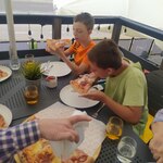 Chłopcy siedzą przy stole i jedzą pizzę.
