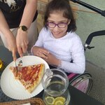 Dziewczynka siedzi przy stole na którym stoi talerz z pizzą.