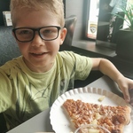 Uczeń siedzi przy stole. Przed nim stoi talerz z pizzą.