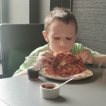 Uczeń siedzi przy stole i je pizzę.