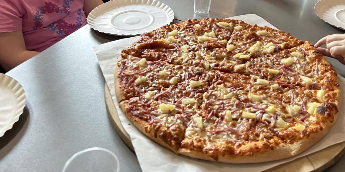 Uczniowie siedzą przy stole. Przed nimi stoi talerz z pizzą.