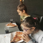 Uczniowie siedzą przy stole i jedzą pizzę.