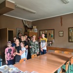 Grupa osób stoi  w sali za stołem.