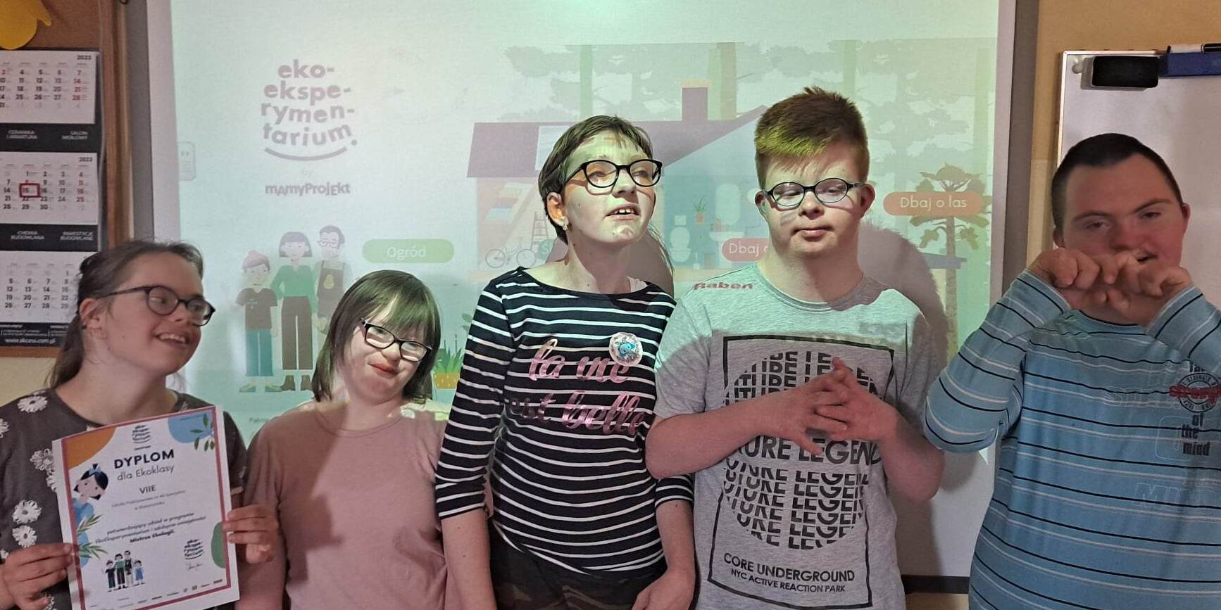 Uczniowie na tle tablicy interaktywnej z dyplomem za udział w projekcie.