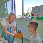 Nauczycielka trzyma tort, uczeń zdmuchuje świeczkę