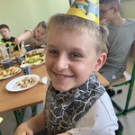 Uśmiechnięty uczeń siedzi przy stole w czapeczce urodzinowej.