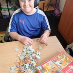 Uczeń siedzi w słuchawkach, układa puzzle