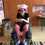 Uśmiechnięta uczennica na wózku w różowej czapce.