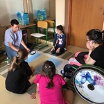 Nauczycielka i uczennice siedzą na dywanie - wykonują dużą pracę plastyczną.