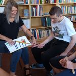 Nauczycielka pokazuje obrazek w książce uczniom siedzącym wokół niej na krzesełkach.