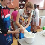 Uczennica i uczeń wlewają mleko z butelki do białej miski stojącej na stole.