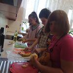 Uczniowie stoją przy blacie kuchennym i obierają jabłka.