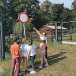 Grupa uczniów patrzy na nauczycielką wskazującą ręką znak drogowy.