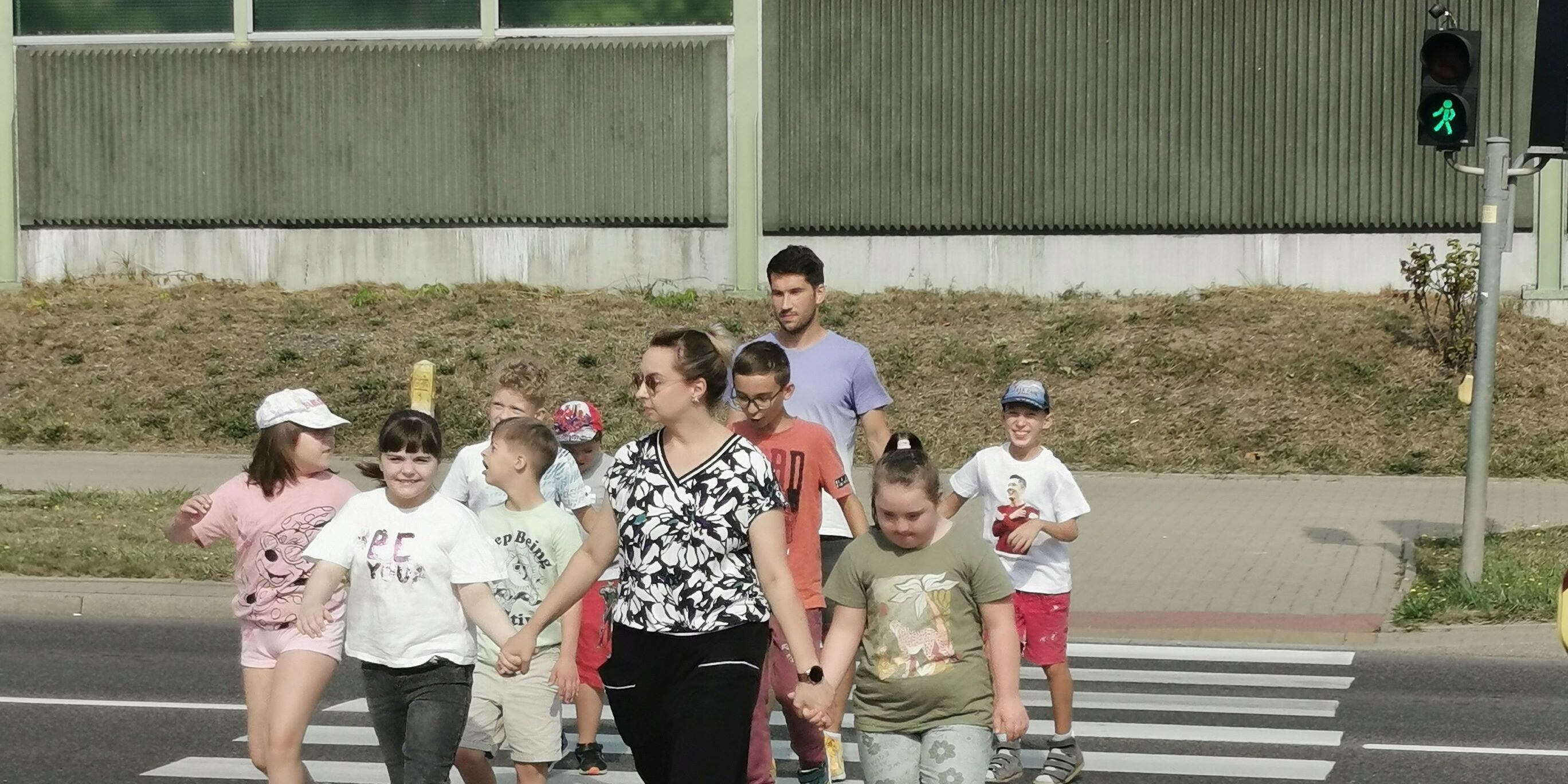 Grupa uczniów z nauczycielami przechodzi przez przejście dla pieszych z sygnalizacją świetlną.