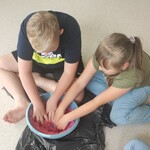 Dwoje uczniów siedzi na podłodze i miesza rękoma różowy piasek w misce