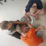 Trójkauczniów siedzi na podłodze i miesza rękoma różowy piasek w misce