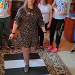 Na dywanie, przed przejściem dla pieszych(stworzonym przez uczniów z kartek papieru ) stoi chłopiec i dwie dziewczynki, obserwując czy dziewczynka we właściwy sposób przechodzi przez przejście.