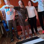 Na dywanie stoją trzy dziewczynki i jeden chłopiec. Uczniowie ćwiczą poprawne rozglądanie się podczas przechodzenia przez pasy. Uczniowie patrzą i wskazują ręka w prawą stronę.