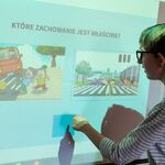 Uczennica na tablicy multimedialnej wskazuje poprawne/ niepoprawne zachowanie na drodze.