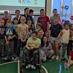 Uczniowie biorący udział w spotkaniu pozują w grupowym zdjęciu z panią policjantką.