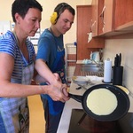 Nauczycielka pomaga uczniowi upiec placek naleśnikowy na patelni.