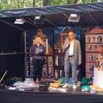 Trzy dorosłe osoby na scenie.W tle trzy kamieniczki.