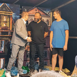 Nauczyciel i uczeń odbierają nagrodę z rąk organizatora na scenie.
