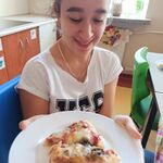 Uśmiechnięta uczennica trzyma przed sobą talerz z pizzą.