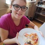 Uśmiechnięta uczennica trzyma przed sobą talerz z pizzą.