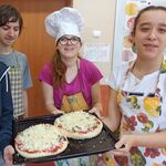 Trójka uczniów trzyma blachę z pizzami.