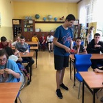 Grupa uczniów siedzi przy ławkach, jeden uczeń stoi