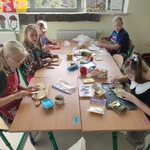 Grupa uczniów siedzi przy stole i przygotowuje kanapki