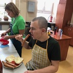 Uczeń je parówkę z widelca. Obok stoi opiekunka.