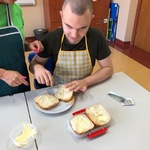 Uczeń smaruje masłem połówkę bułki. Obok stoi nauczycielka.