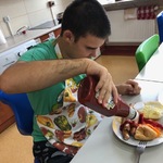 Uczeń siedzi przy stole i nalewa ketchup z butelki na potrawę znajdującą się na talerzu stojącym przed nim na stole.