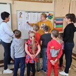 Nauczycielka wskazuje obrazki powieszona na tablicy grupie uczniów.