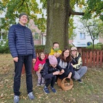 Nauczycielka i grupa uczniów przykucnięta pod drzewem. Obok stoi uczeń
