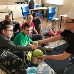 Grupa uczniów patrzy na uczennicę, która  miesza warzywa w dużym garnku trzymanym przez nauczycielkę.