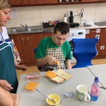 Uczeń siedzi przy stole i kładzie ser na tost leżący na talerzu.