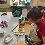 Uczeń siedzi przy stole i kładzie plasterki sera na tosty leżące przed nim na talerzu.