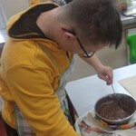 Uczeń miesza łyżką ciasto w garnku.