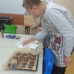 Uczeń posypuje posypka ciasteczka leżące na blaszce.