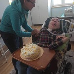 Chłopiec na wózku z tortem. Na torcie napis: 22 lata. Obok stoi nauczycielka.