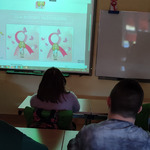 Uczniowie siedzą w ławkach, naprzeciw nich włączona jest tablica multimedialna. Uczniowie słuchają informacji na temat: „Różowy Październik”.