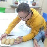 Uczeń stawia przed kolegą talerz z bułkami.
