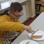 Uczeń siedzi przy stole i ponosi parówkę szczypcami.