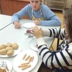 Uczeń i uczennica siedzą przy stole na którym stoją talerze z produktami do wykonania hot doga.